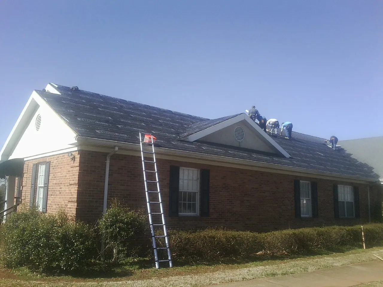 Crew tearing shingles off a brick ranch roof with a ladder set — Metal Roof Repair work by our crew in Crofton