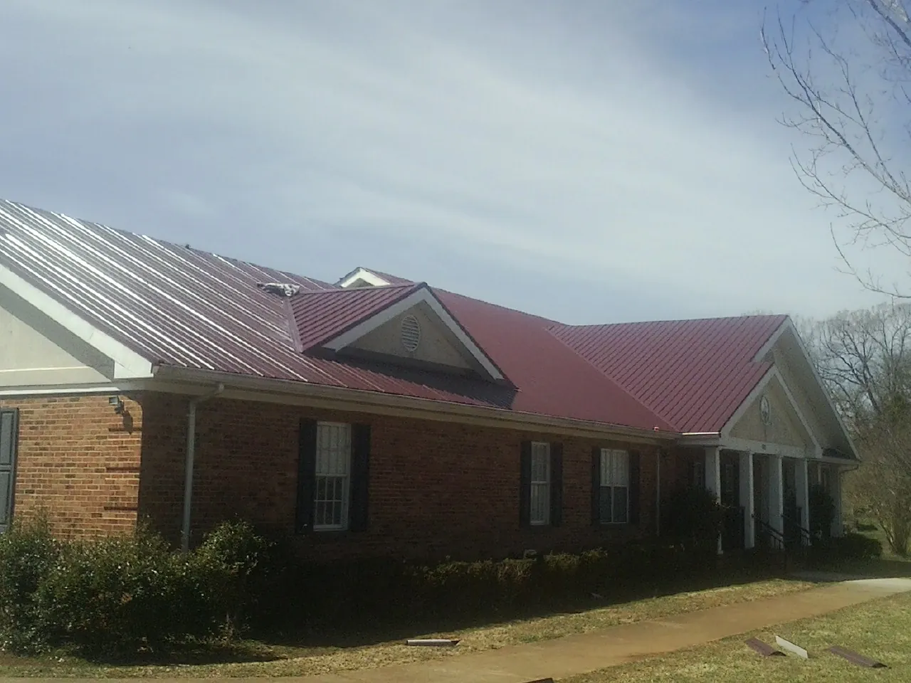 Red metal roof with gabled entries on a long brick building, from a Hail Damage Roof Repair job in Crofton