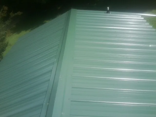 New green metal panels meeting at the ridge of a roof — Flat Roof Repair work by our crew in Crofton