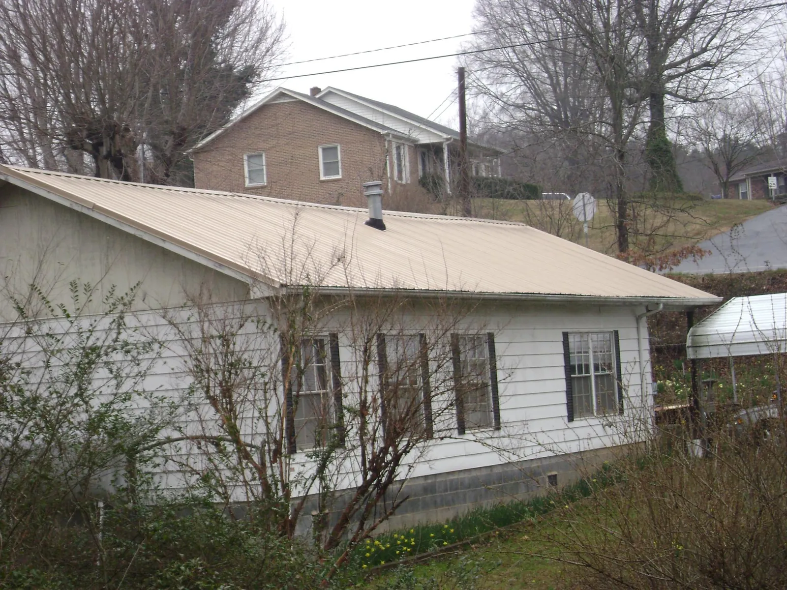 Tan metal roof on a white sided house set into a hillside — Commercial Roofing by Roofing Brothers in Crofton